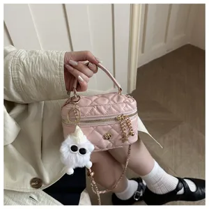 Detalle de bolso cruzado cilíndrico acolchado rosa con cadena y abalorio de felpa.