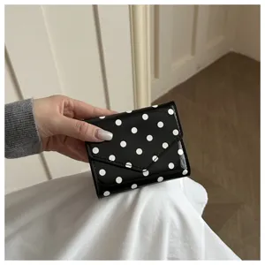 Detail shot of a chic black and white polka dot compact wallet, showing glossy texture.