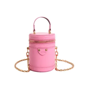 Sac bandoulière cylindrique rose avec poignée et chaîne dorée, mini sac en cuir verni.