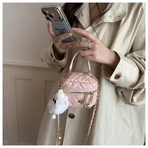 Detalle de mini bolso cruzado acolchado rosa con dije blanco esponjoso y correa de cadena.