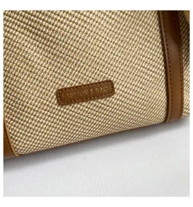 Vista detallada del bolso tote de lona tejida con ribete de cuero marrón y etiqueta de moda.