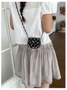 Detailansicht einer süßen schwarz-weißen Pünktchen-Mini-Satteltasche mit Schultergurt im Tragemodus.