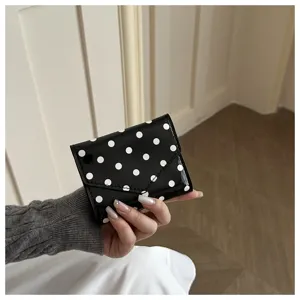 Close-up detail of black and white polka dot patent leather wallet, elegant folding design.