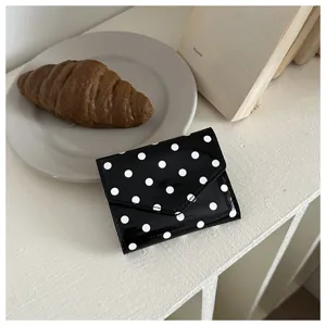 Primo piano dettagliato di un mini portafoglio chic a pois neri e bianchi su fondo bianco.