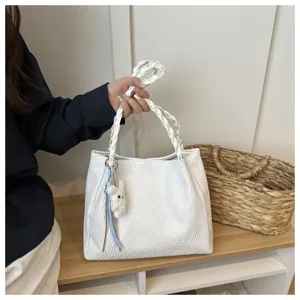 Detailed view of the white woven tote bag featuring a cute plush bear charm and chic handle.