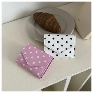 Close-up detail shot of cute polka dot mini wallets in pink and white on styled desktop.
