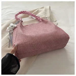 Detailed view of the pink woven shoulder bag with cute bear pendant and braided handle.