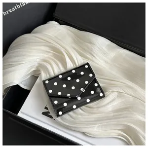 Close-up detail view of black and white polka dot mini wallet card holder in stylish box.