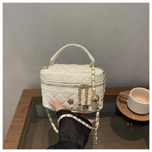 Detalle de bolso bandolera acolchado blanco con correa de cadena dorada y dije de camelia.