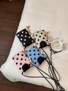 Vue de détail en gros plan de sacs à bandoulière à pois élégants dans plusieurs couleurs sur lit.