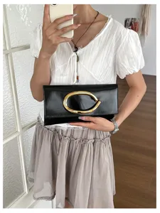 Details van minimalistische zwarte envelopclutch met opvallende gouden C-vormige gesp.