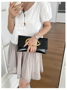 Minimalistische zwarte enveloppe tas voor dames met luxe gouden metalen C-handvat ontwerp.