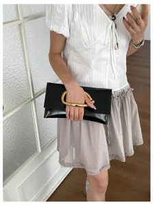 Minimalistische zwarte lakleren clutch tas met elegante gouden metalen handgreep voor dames.