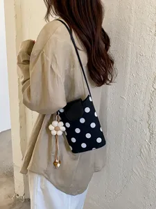 Détail élégant de sac bandoulière à pois noirs et blancs avec rabat stylé et charmant pendentif.