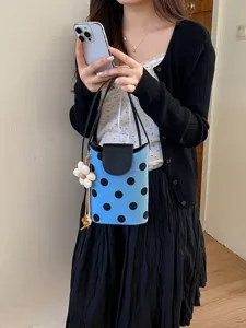 Détail de sac seau à pois bleu et noir, sac bandoulière tendance avec pendentif fleur.
