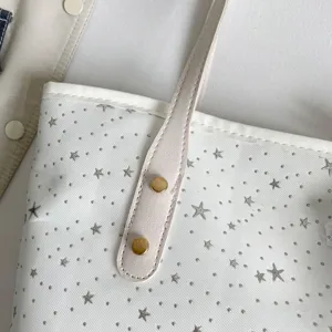 Nahaufnahme der weißen Canvas-Tasche mit silbernem Sternenmuster und goldenen Nieten.