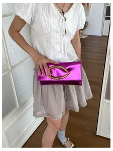 Detailopname van de metallics fuchsia enveloppe clutch met opvallend gouden C-vormig handvat.