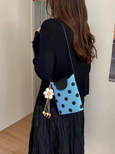 Détail d'un sac bandoulière bleu à pois avec rabat noir et charm fleur porté sur l'épaule.