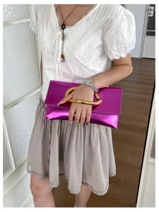 Detail van de metalliek paarse envelop clutch tas met opvallende gouden C-vormige handgreep.
