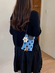 Détail élégant de sac bandoulière à pois bleus, avec un joli pendentif floral tendance.