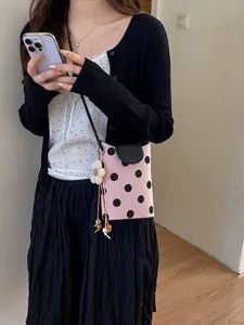 Gros plan du sac bandoulière pour téléphone à pois roses avec pendentif fleur femme.