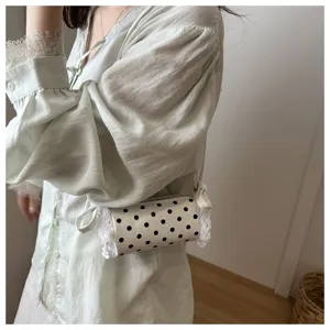 Dettaglio in primo piano di una borsa a tracolla cilindrica a pois per bambina con pizzo bianco.