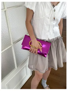 Detailopname van een metallic fuchsia clutch met een opvallend gouden C-vormig handvat.