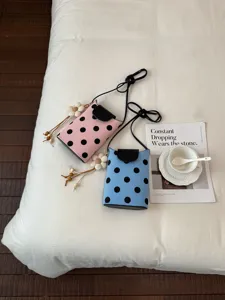 Gros plan du sac bandoulière à pois avec charm fleur et design de rabat noir chic.