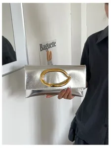 Zilveren metallieke envelop clutch tas met opvallende gouden C-vormige gesp detail.