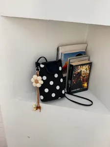 Sac bandoulière à pois noir et blanc, détail avec joli pendentif floral et sangle fine élégante.