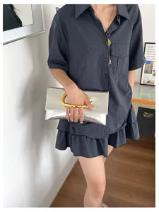 Detailopname van metalen zilveren clutch tas met uniek C-vormig gouden handvat.