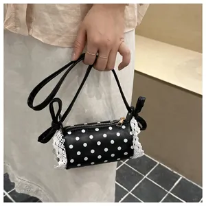 Borsa a tracolla cilindrica a pois neri e bianchi con finiture in pizzo bianco e dettagli a fiocco.
