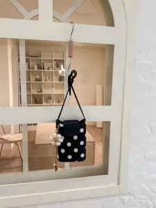 Petit sac bandoulière à pois noir et blanc avec joli pendentif fleur pour les vacances d'été.