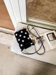 Petit sac bandoulière tendance en toile à pois noirs et blancs avec rabat en cuir pour femmes.