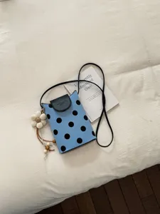 Détail du mini sac à bandoulière à pois bleus, avec rabat noir et joli pendentif de fleur.