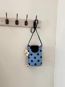 Vue détaillée d'un sac bandoulière bleu à pois noirs, rabat et joli pendentif en forme de fleur.