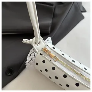 Primo piano dettagliato della borsa cilindrica a pois bianchi con pizzo e cerniera dorata.