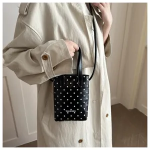 Vista detallada de un mini bolso negro de lunares con correa usado con una gabardina.