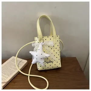 Vista detallada de bolso mini amarillo de lunares con colgante estrella de peluche y lazo encaje.