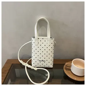 Vista de cerca de un mini bolso de hombro blanco elegante con un diseño de lunares negros.