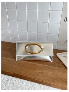 Minimalistische zilveren metallic envelop clutch tas met gouden C-vormige gesp detail.