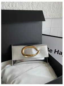 Gedetailleerd opname van zilveren metallic clutch met gouden C-handvat in geschenkdoos.