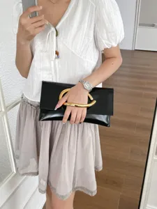 Elegante zwarte enveloppe clutch tas voor dames met opvallende gouden C-vormige metalen handgreep.