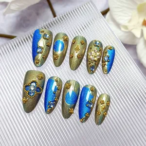 Detalle de uñas postizas azules ojo de gato hechas a mano, relieve dorado barroco y pedrería.