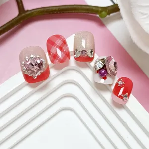 Primer plano de uñas postizas hechas a mano con cuadros rojos, efecto ojo de gato y pedrería.