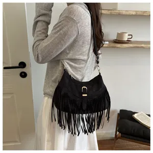 Detailed shot of a black suede fringe shoulder bag worn by a model in a cozy room setting.
