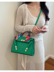 Green ostrich pattern leather top handle crossbody bag detail view with scarf and metal lock.