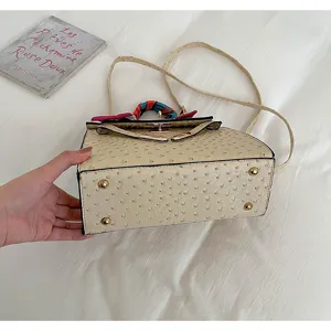 Beige faux ostrich leather handbag with scarf detail, top handle and crossbody strap.