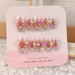 Primer plano detallado de uñas postizas hechas a mano con base degradada y pedrería.