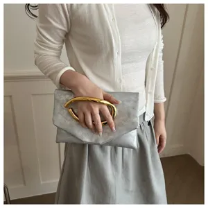 Silver metallic clutch bag with a bold curved gold handle, chic niche design for women.